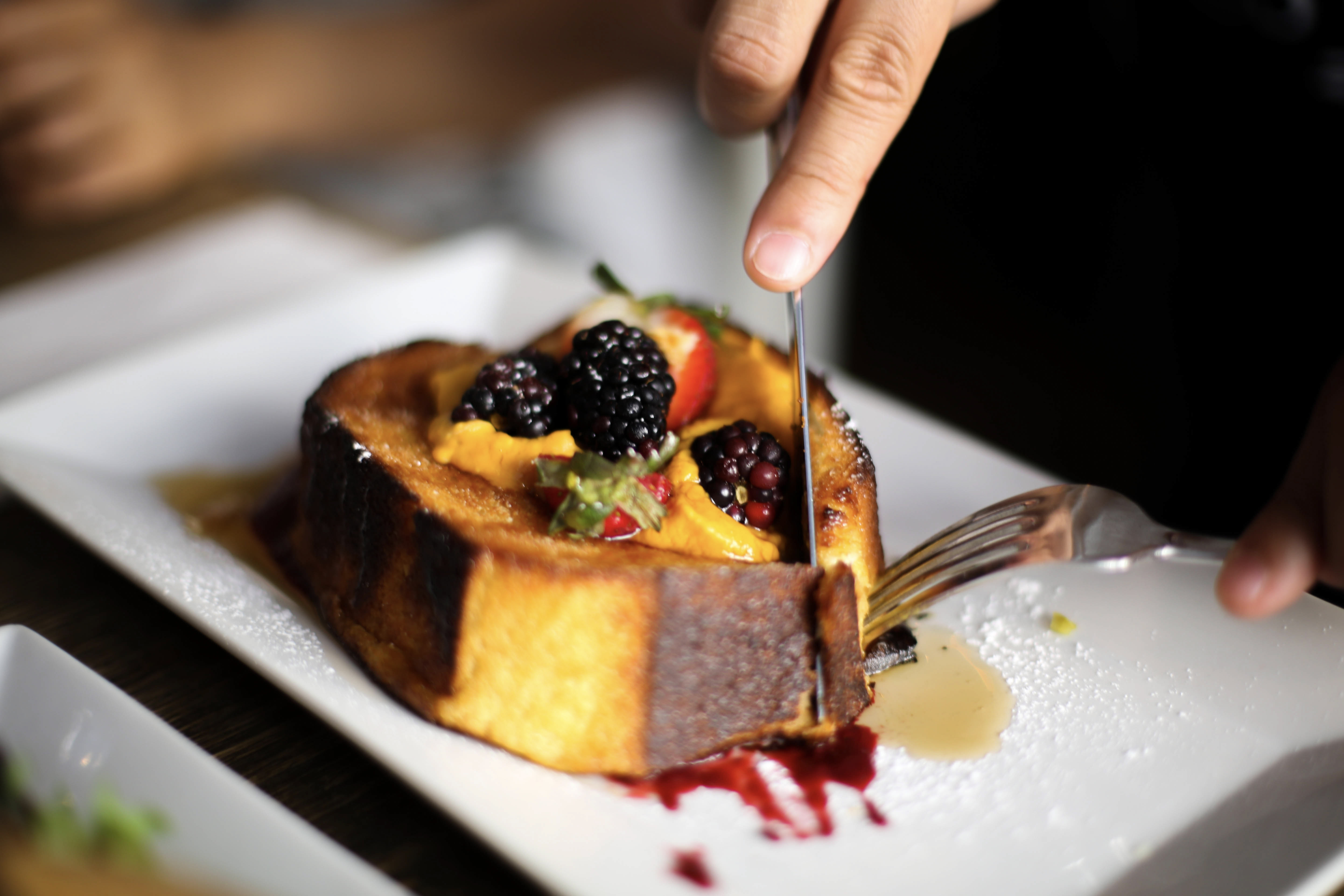 Thick golden French toast topped with blackberries, strawberries, and cream on a white plate