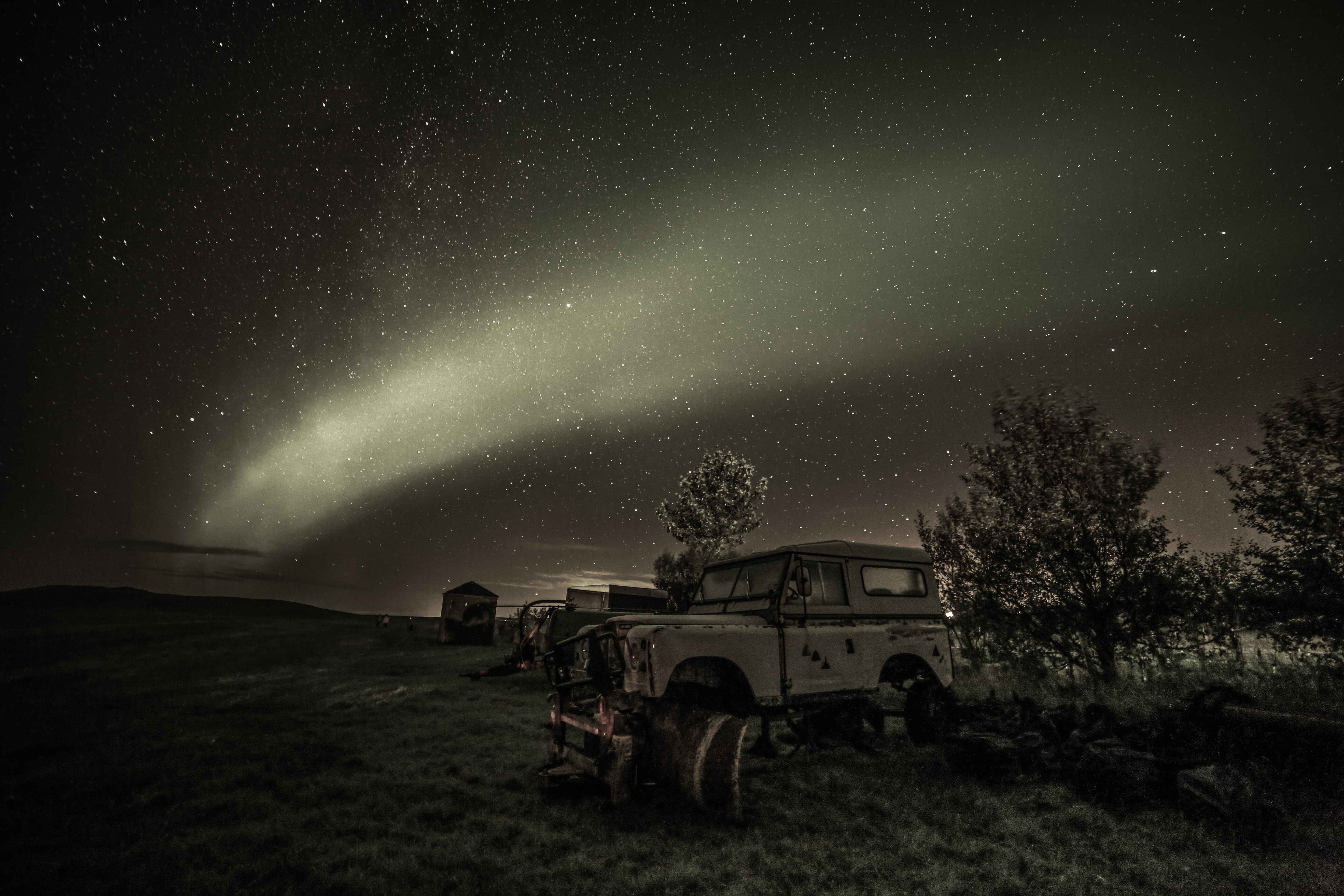 Abandoned off-road vehicle under a green aurora and starry sky in a grassy field