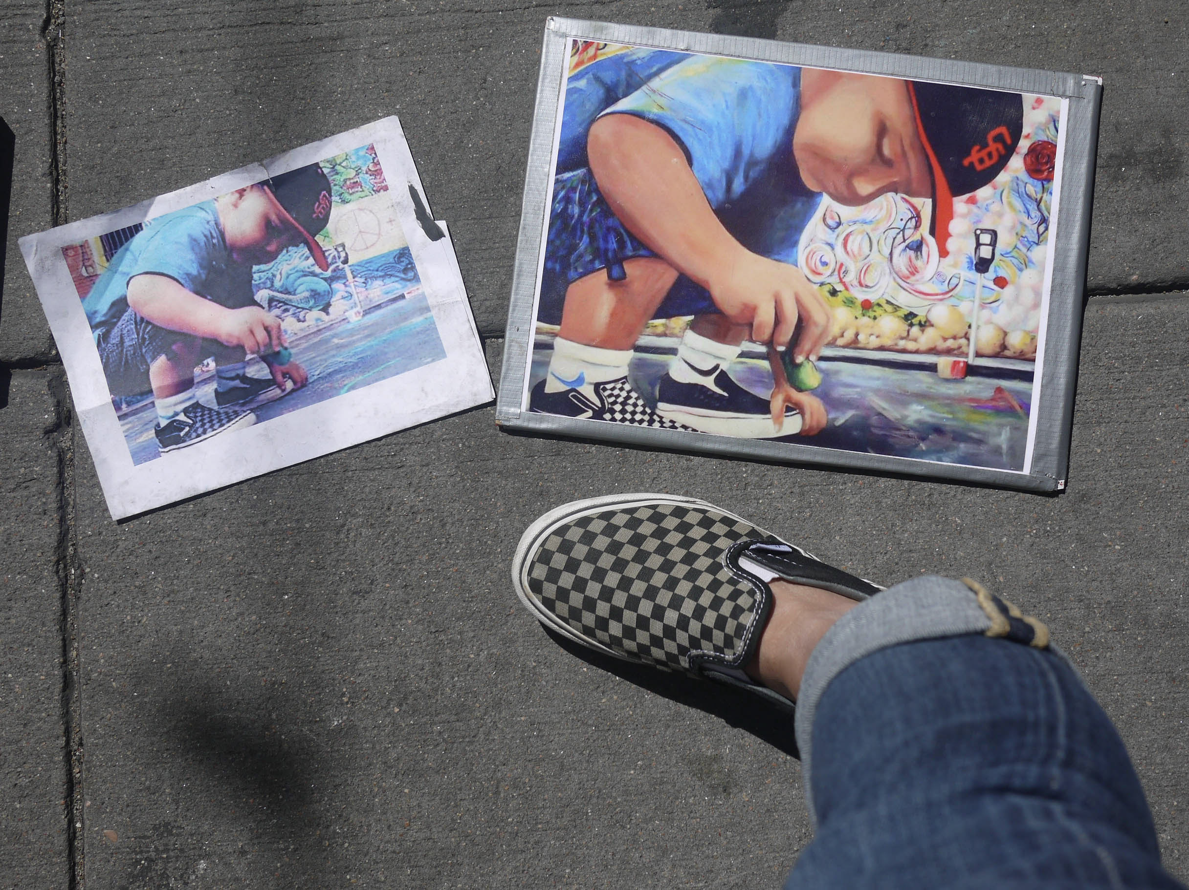 Checkered slip-on shoe and rolled jeans on a gray sidewalk beside two taped art prints of a child drawing with chalk